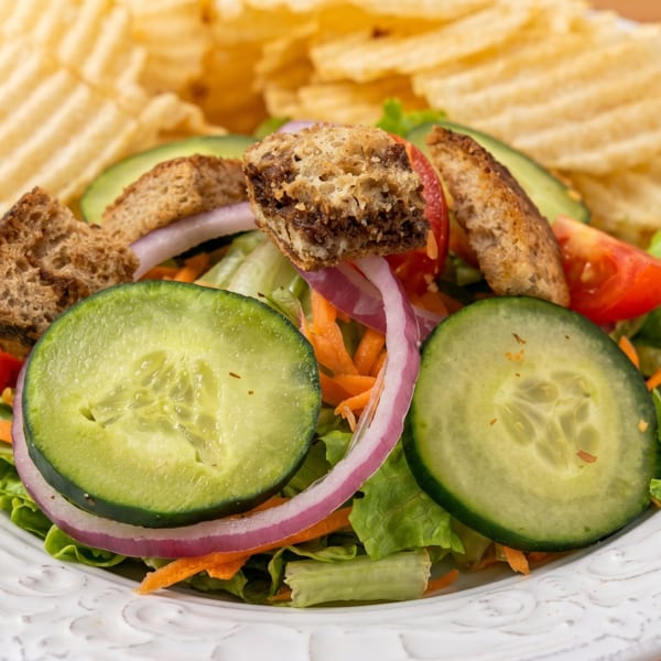 Fresh garden salad with cucumbers, tomatoes, red onion, croutons, and a side of potato chips.