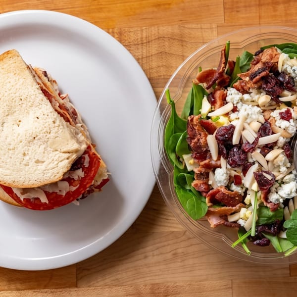 A sandwich on white bread and a salad with spinach, bacon, cranberries, and almonds.